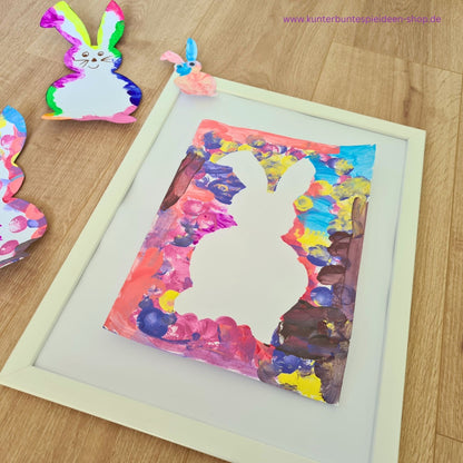 Bunt gestaltetes Osterbild mit weißer Hasen-Silhouette im Rahmen. Die Osterhase Kontur Vorlage zum Ausdrucken wurde hier als kreative Osteridee für Kinder mit Farbe umgesetzt.