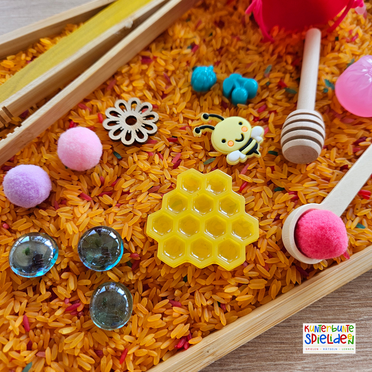 Sensorisches Spiel Biene und ihre Honigwabe für ein Sensory Play Aktionstablett nach Maria Montessori im Sommer. Sensorik-Spielset für Kinder, bestehend aus sensorischem Reis, bunt gefärbt . Das Sensory Play beinhaltet verschiedene Schüttwerkzeuge wie eine Zange und einen Löffel, eine detailgetreue, aus Resin gegossene Honigwabe und weitere lose Teile zur Förderung der Feinmotorik und sensorischen Wahrnehmung. Ideal für spielerisches Lernen und Entdecken im Kindergarten oder zu Hause.