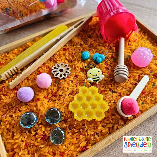Sensorisches Spiel Biene und ihre Honigwabe für Aktionstablett nach Maria Montessori im Sommer. Sensorik-Spielset für Kinder, bestehend aus sensorischem Reis, bunt gefärbt . Das Sensory Play beinhaltet verschiedene Schüttwerkzeuge wie eine Zange und einen Löffel, eine detailgetreue, aus Resin gegossene Honigwabe und weitere lose Teile zur Förderung der Feinmotorik und sensorischen Wahrnehmung. Ideal für spielerisches Lernen und Entdecken im Kindergarten oder zu Hause.