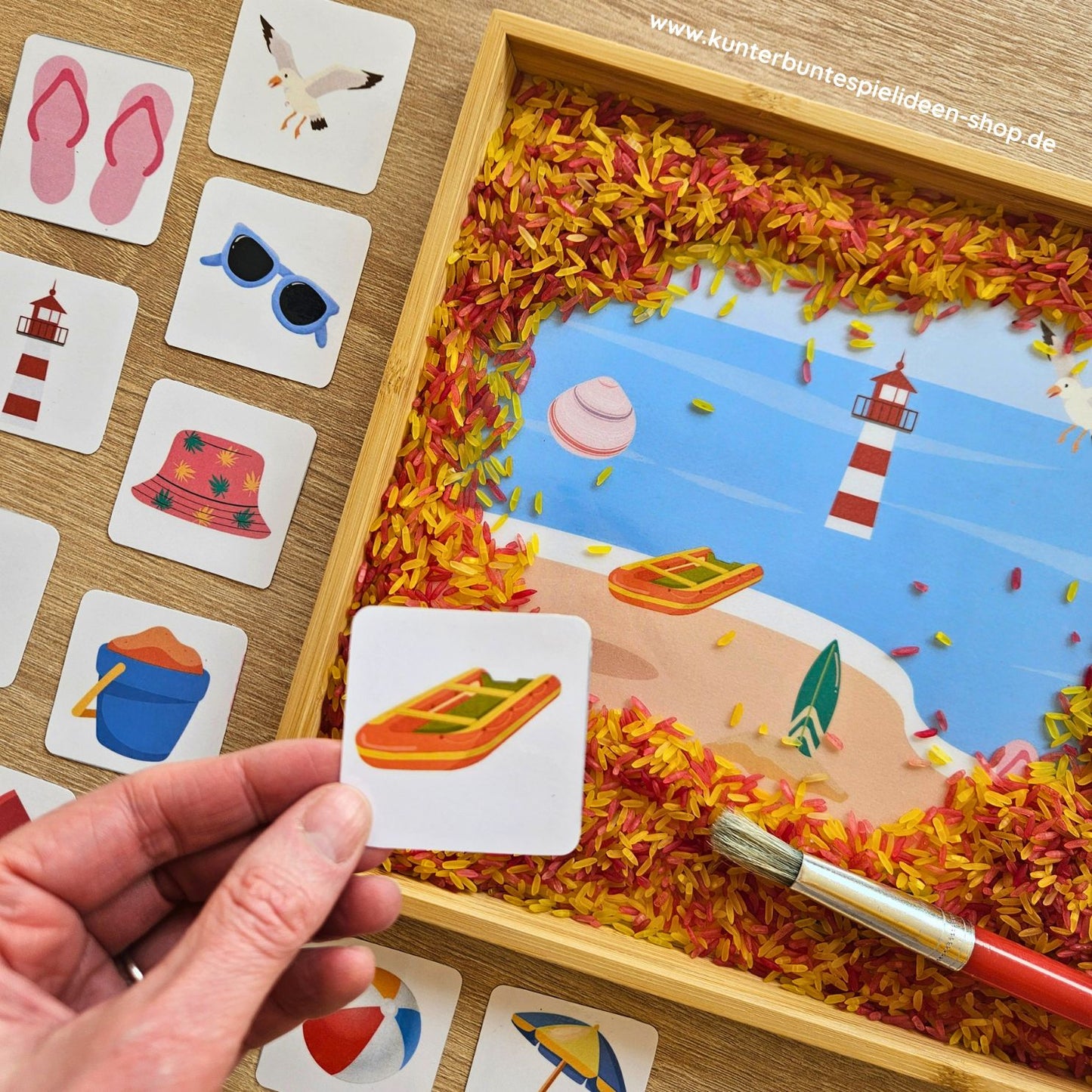 Sommerliches Suchbild für Kinder: In einer Box mit buntem Reis sind Strandmotive wie Boot, Muschel und Leuchtturm versteckt, ergänzt durch passende Bildkarten
Sensorik-Spiel „Sommer am Strand“ – Kinder entdecken versteckte Objekte im Reis und ordnen sie den Karten zu
Kreatives Lernspiel für Kinder zum Thema Strand: Suchbild mit buntem Reis, Bildkarten und sommerlichen Motiven