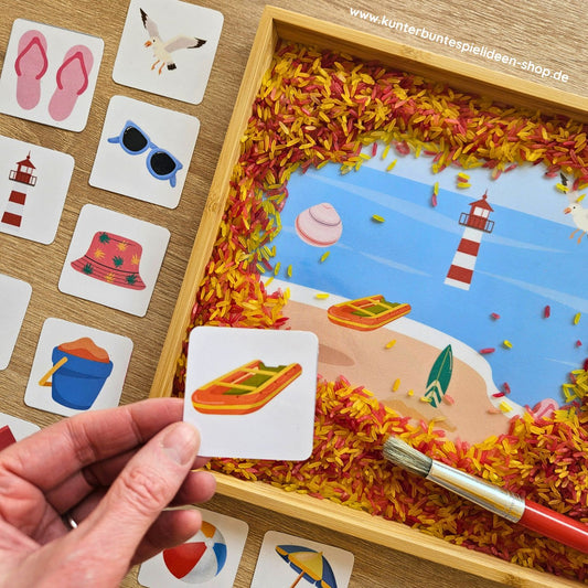 Sommerliches Suchbild für Kinder: In einer Box mit buntem Reis sind Strandmotive wie Boot, Muschel und Leuchtturm versteckt, ergänzt durch passende Bildkarten
Sensorik-Spiel „Sommer am Strand“ – Kinder entdecken versteckte Objekte im Reis und ordnen sie den Karten zu
Kreatives Lernspiel für Kinder zum Thema Strand: Suchbild mit buntem Reis, Bildkarten und sommerlichen Motiven