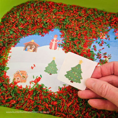 Suchen-und-Finden zu Weihnachten im Aktionstablett: Hand entdeckt den Weihnachtsbaum im rot-grünen Spielreis; weihnachtliche Symbole wie Krippe und Nikolaus sichtbar – Sensory Play als Montessori Kinderhaus-Material zur Feinmotorik und Sprachförderung (der/die/das).