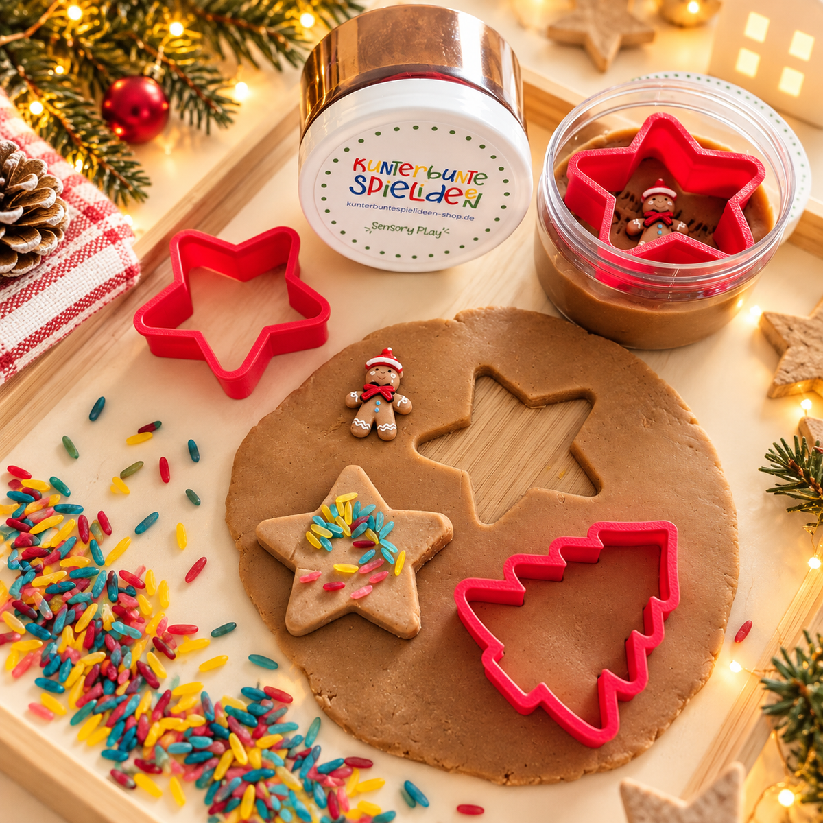 Weihnachtsbäckerei spielen mit Kindern – Knete in der Dose, rote Ausstechformen für Stern und Tannenbaum und bunte Streusel zum Gestalten eigener Knetplätzchen.