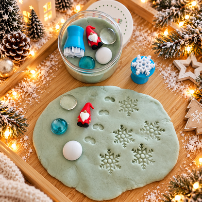 Wichtelgeschenk mit veganer Schneeknete in der Dose, kleiner Wichtelfigur, Schneeflockenstempel und winterlichen Muggelsteinen auf einem weihnachtlich dekorierten Holztisch.