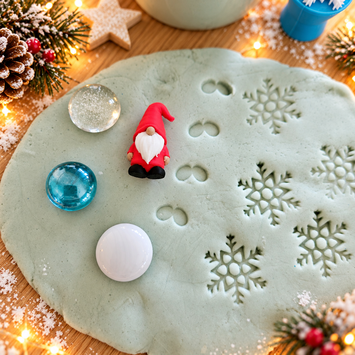 Winterliches Knetset für Kinder mit ausgerollter veganer Schneeknete, Schneeflockenabdrücken, kleiner Wichtelfigur und drei Muggelsteinen in Weiß, Türkis und Transparent.