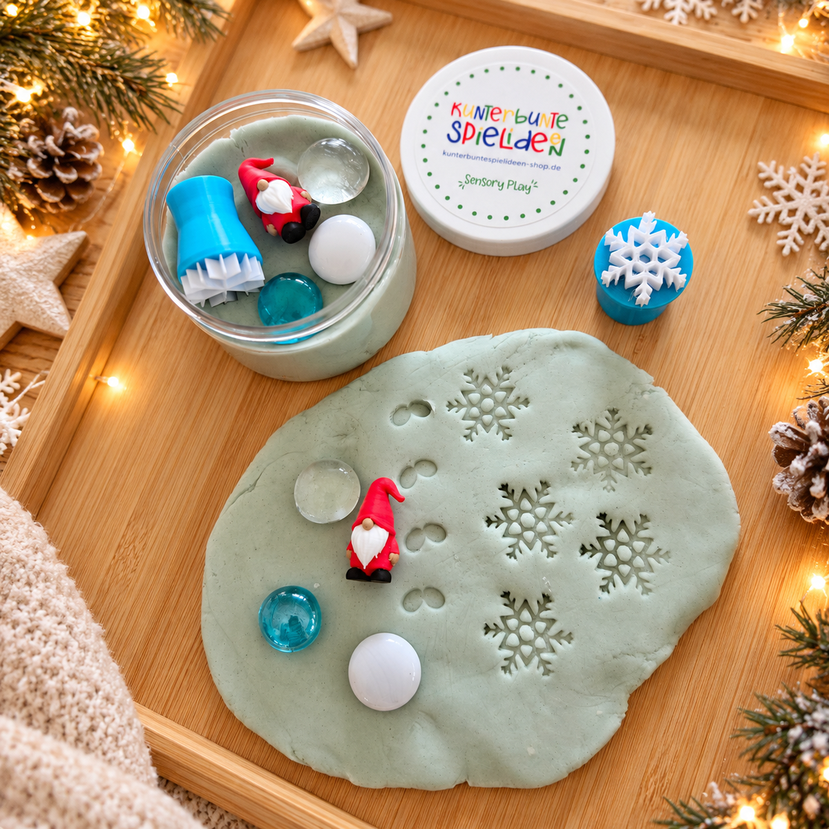 Kreatives Wichtelgeschenk für Kinder mit Schneeknete, Schneeflockenstempel und Muggelsteinen auf einem weihnachtlich geschmückten Holztablett.