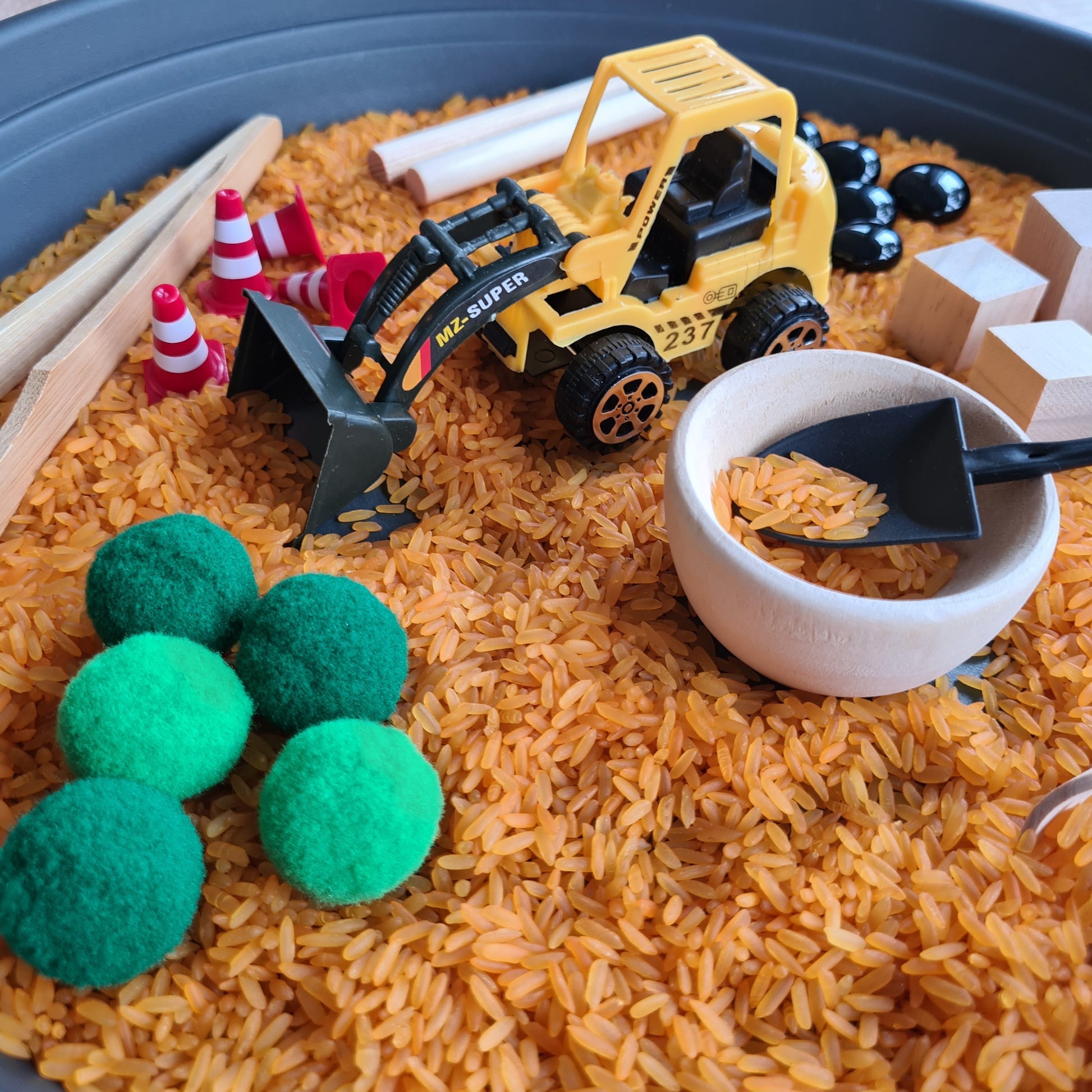 Montessori Sinnesspiel Baustelle mit sensorischem Reis, Baustellenfahrzeug, Schüttwerkzeugen und losen Materialien für Schüttspiele und Sensory Play. Sensorisches Spiel für Kinder zur Förderung von Feinmotorik, Konzentration, Sinnesförderung und kreativem Entdecken.